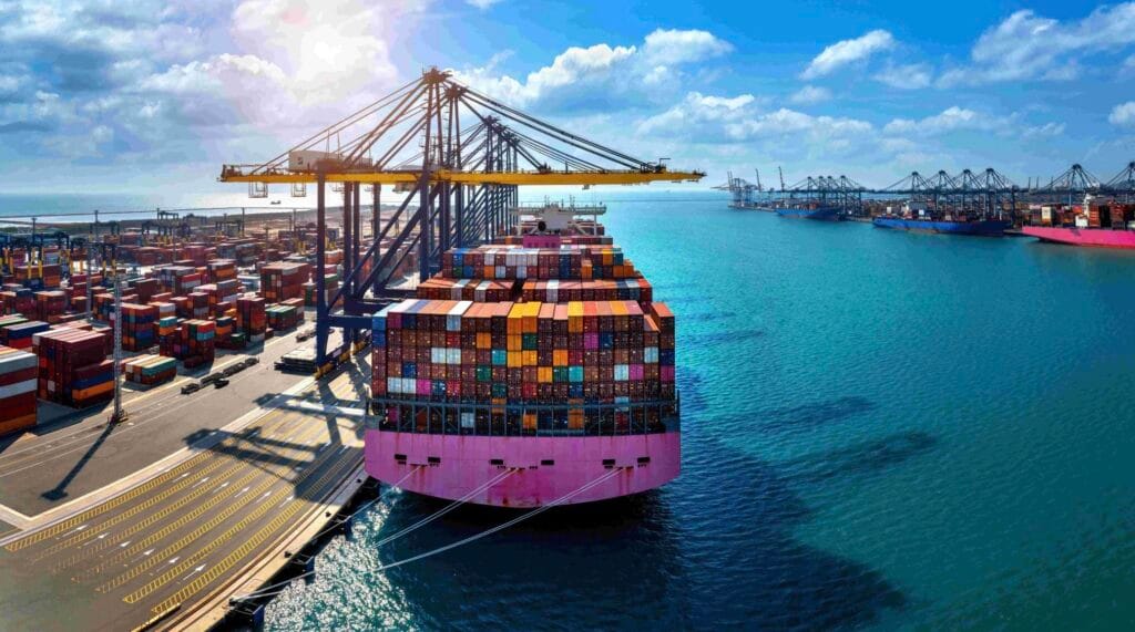 Large container ship docked at Kandla port, stacked with colorful shipping containers and cranes along the waterfront.