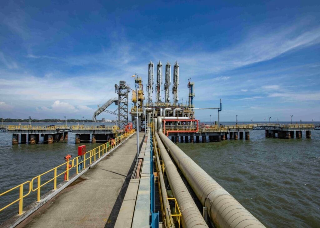 Petronet LNG’s Kochi LNG terminal jetty with gas pipelines and unloading infrastructure extending into the sea under a clear blue sky.