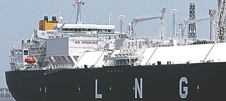 Liquefied natural gas (LNG) tanker docked at an industrial port with large LNG storage tanks and loading infrastructure visible.